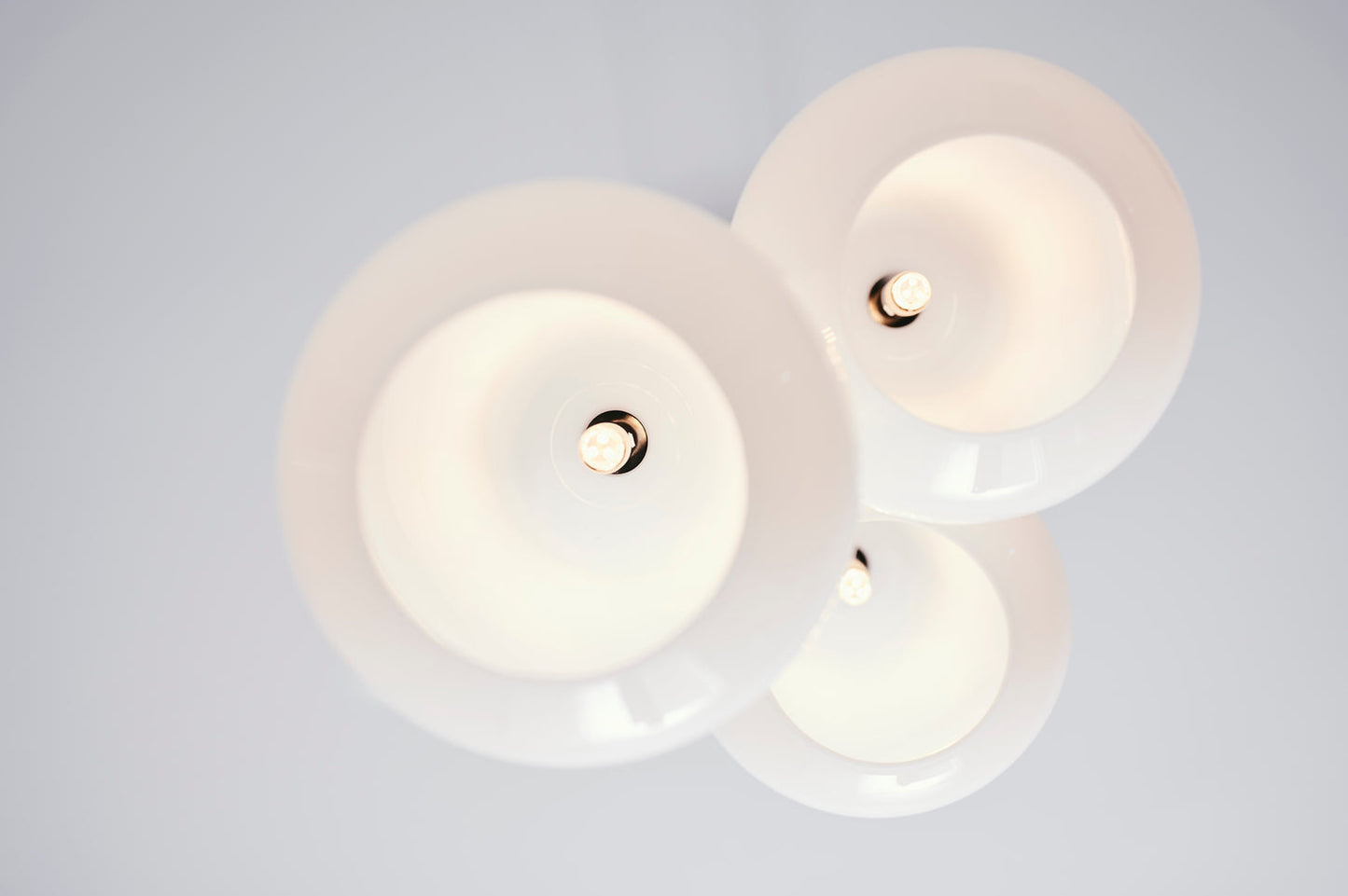 Pendel bestående af tre dråbeformede skærme af opalglas med gyldent ophæng og hvid ledning, set nedefra