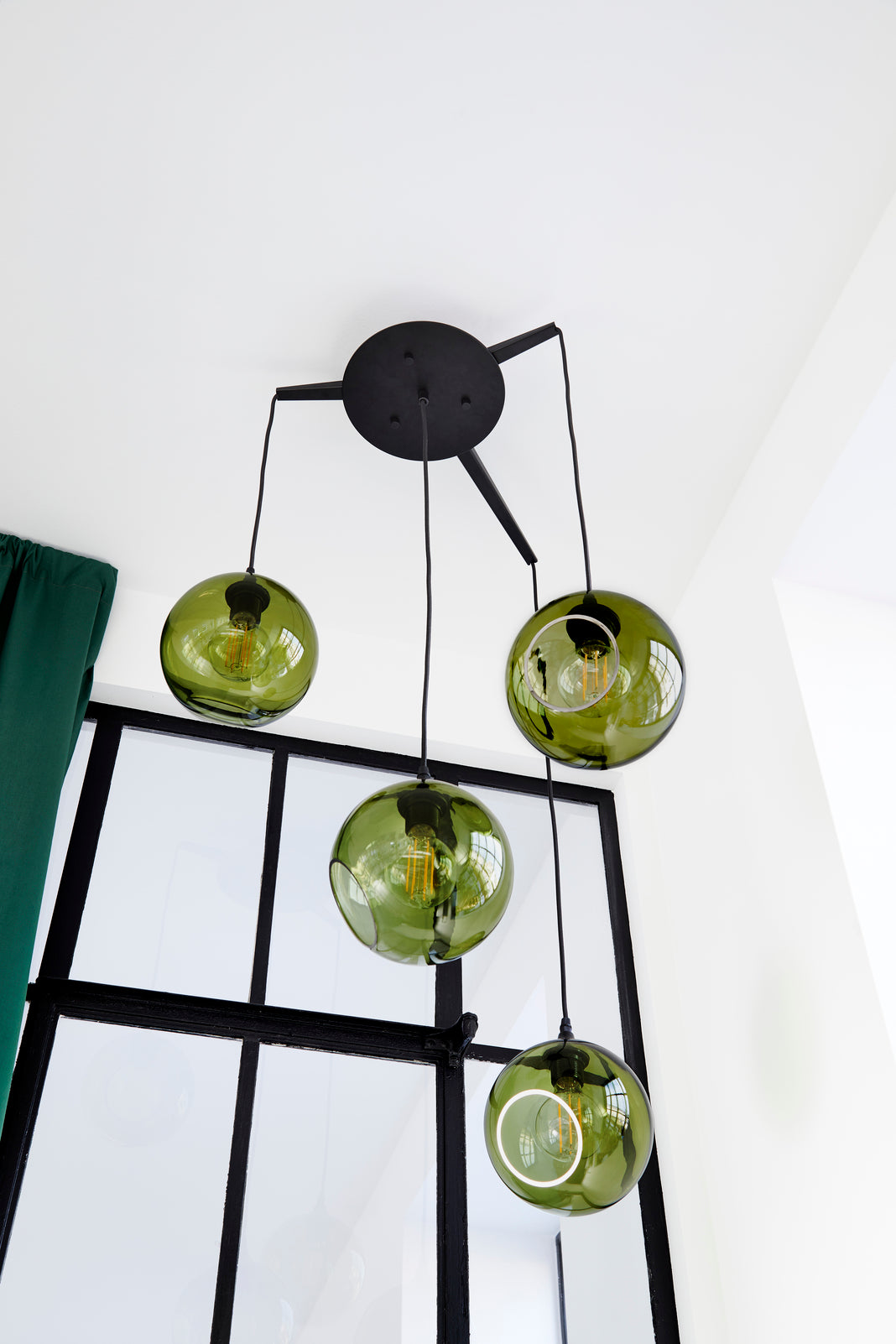 Rund lampe i grøn glas med et afskåret stykke med kig til pæren. Fatning er sort og ledningen er af sort stof.