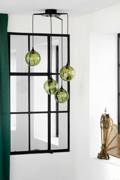 Rund lampe i grøn glas med et afskåret stykke med kig til pæren. Fatning er sort og ledningen er af sort stof.