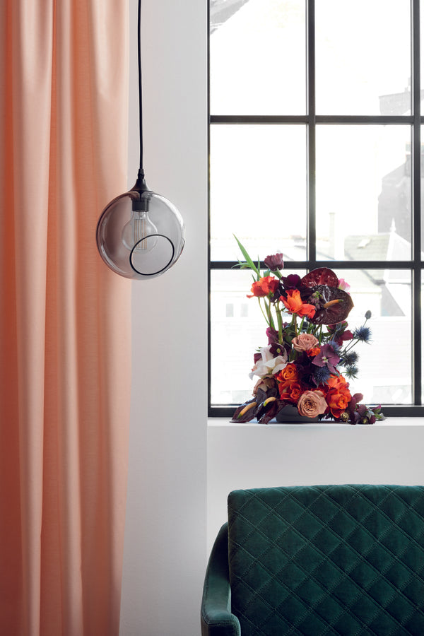 Rund pendel lampe i smoked glas med et afskåret stykke med kig til pæren. Fatning er sort og ledningen er af sort stof.